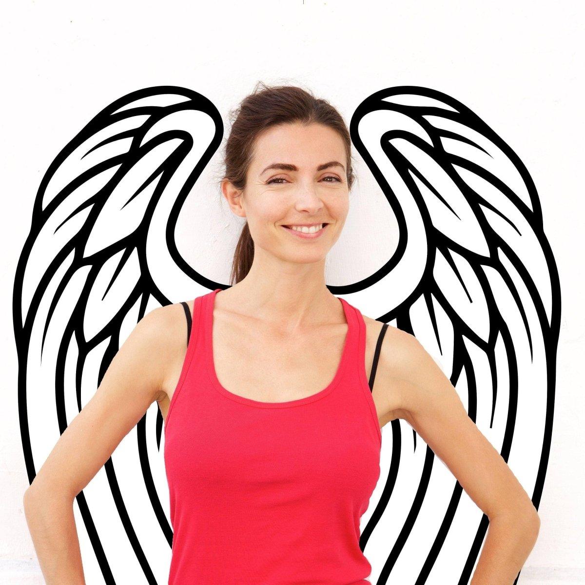 Smiling woman in red tank top with decorative angel wings wall decor behind her, showcasing bohemian style.