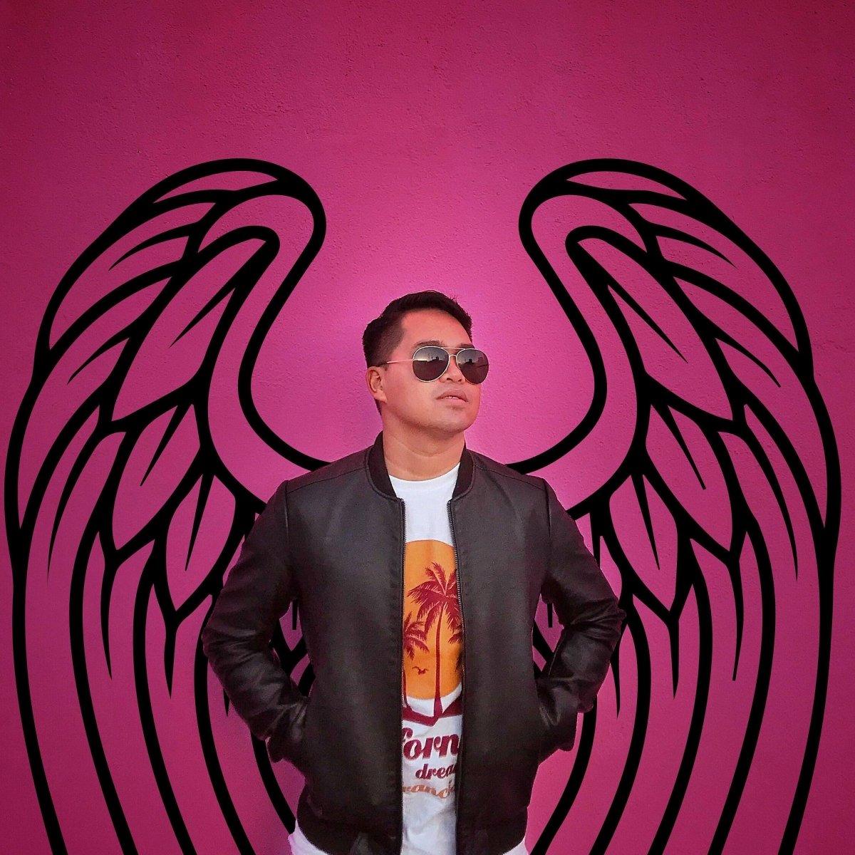 Person in sunglasses standing confidently in front of pink angel wings mural, showcasing urban style and creativity.