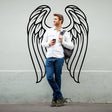 Man standing next to feathered angel wings wall decor, showcasing a stylish and bohemian wall art design.