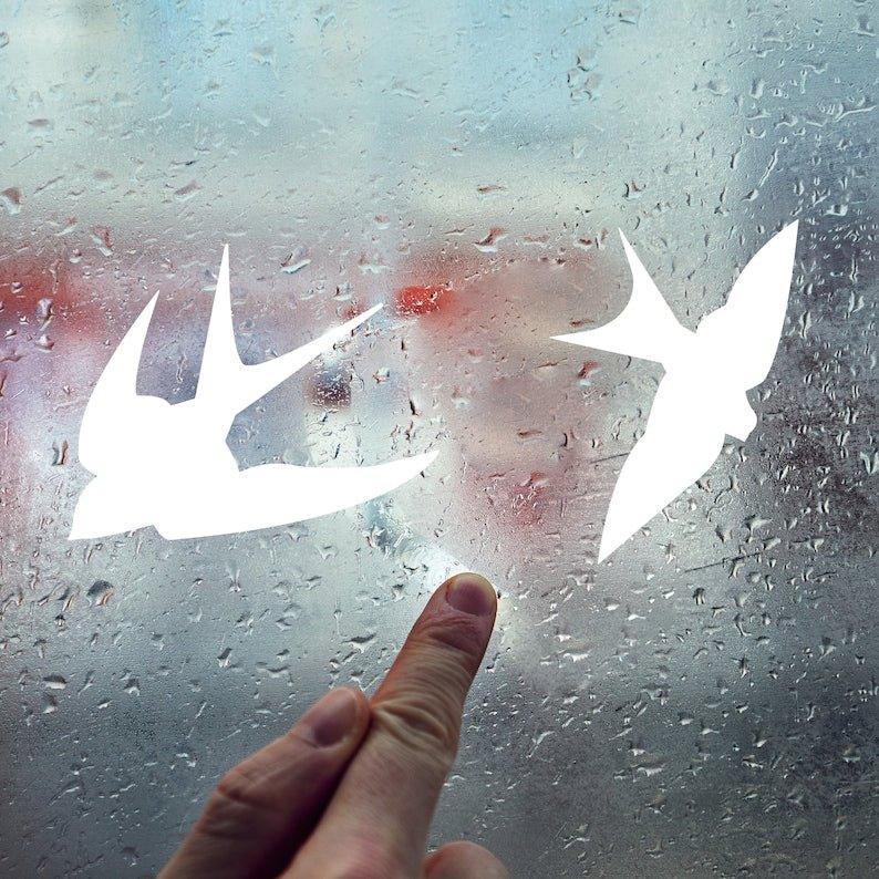 Person pointing at FeatherGuard anti-collision bird decals on a rain-speckled window.