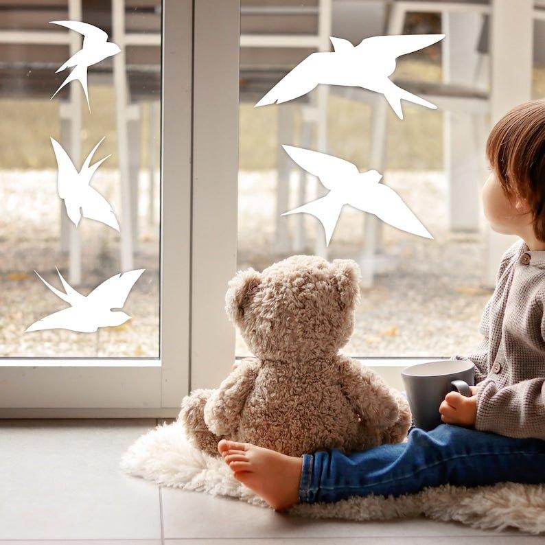 Child sitting with teddy bear by window adorned with FeatherGuard bird protection decals.