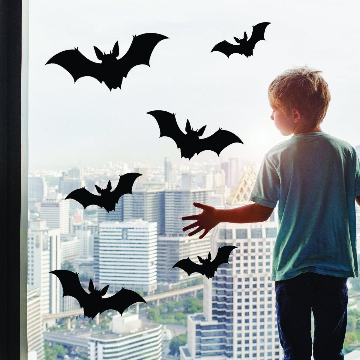 Child admiring Halloween bat decals on window, adding spooky charm to city view for Halloween decorations.