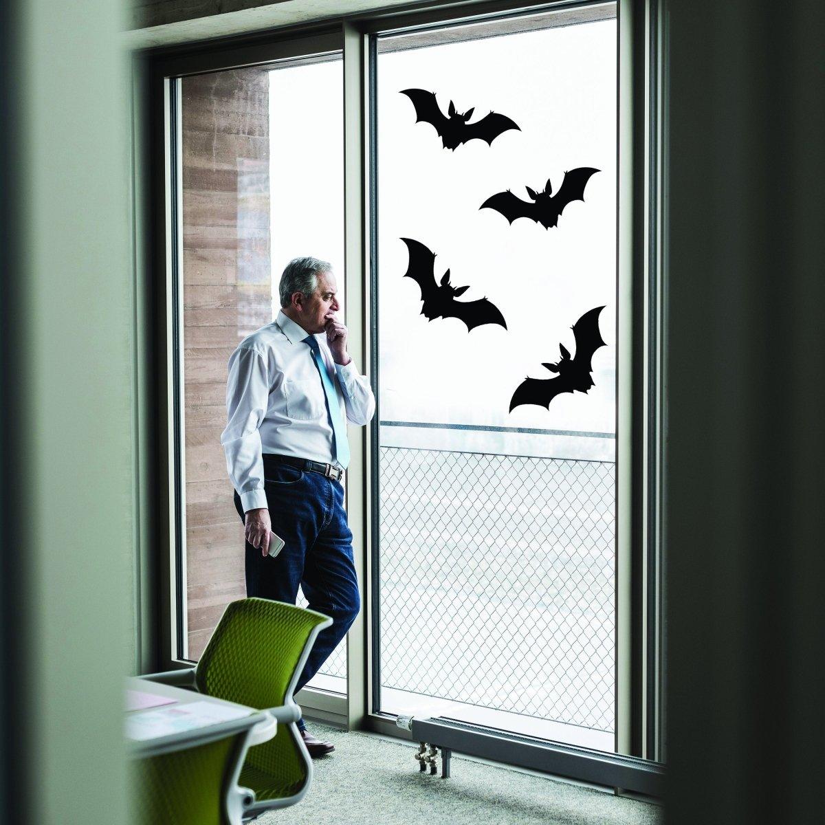 Man standing by a window with Halloween bat decals, adding spooky charm to his office decor.