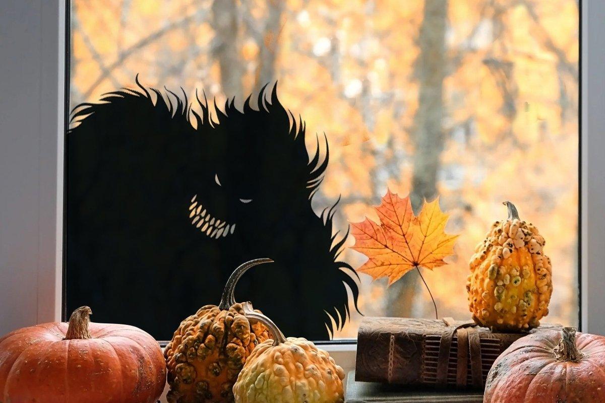 Spooky monster silhouette vinyl decal on window with pumpkins and autumn leaves, perfect for Halloween decor.