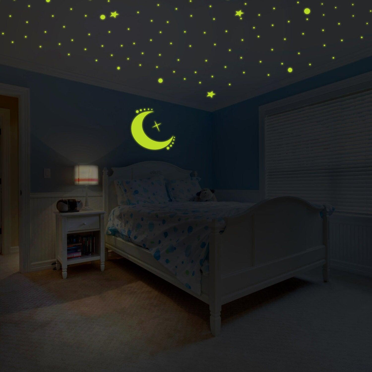Glowing vinyl wall decal of a moon and stars on a dark ceiling in a cozy bedroom.
