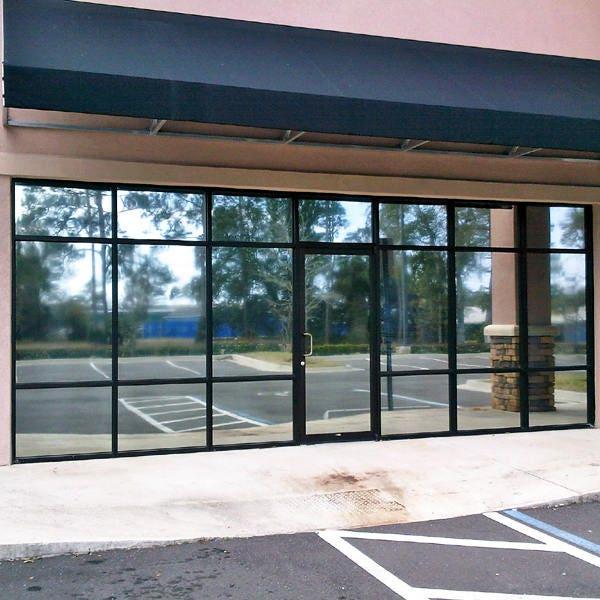 Exterior view of a store with large glass windows and a black awning, surrounded by trees and parking area.