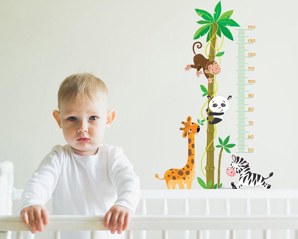 Cute child next to whimsical height growth chart with animals for nursery decor, featuring a monkey, panda, giraffe, and zebra.