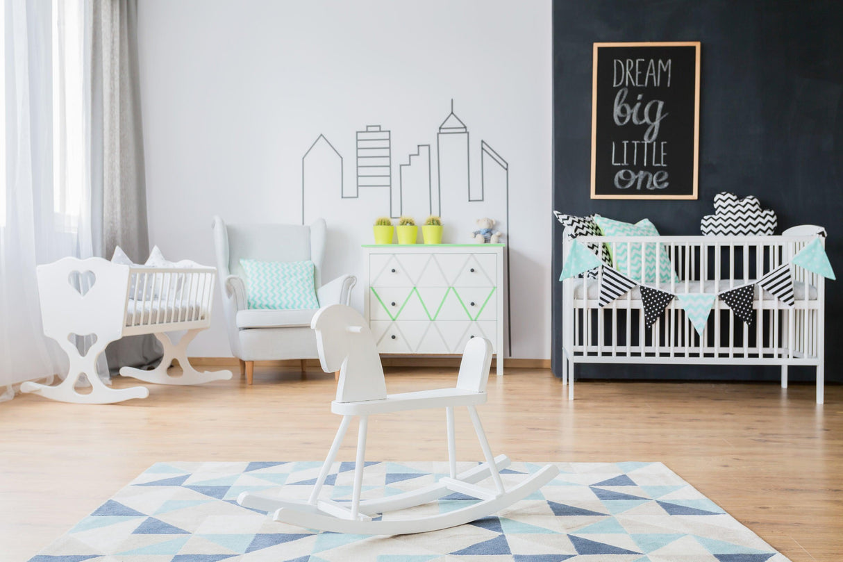 Stylish nursery featuring white furniture, a rocking horse, and wall decorations with a motivational quote.