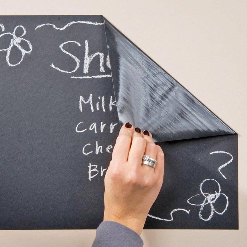 Hand peeling back a corner of a chalkboard wall sticker featuring handwritten notes and doodles.