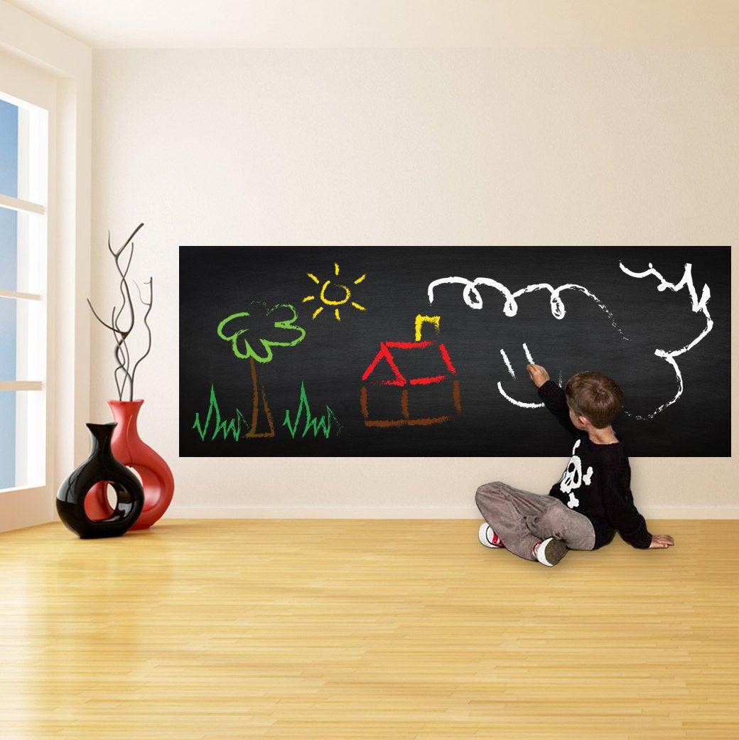 Child drawing on black chalkboard wall decal in a bright living space, showcasing creativity with chalk.