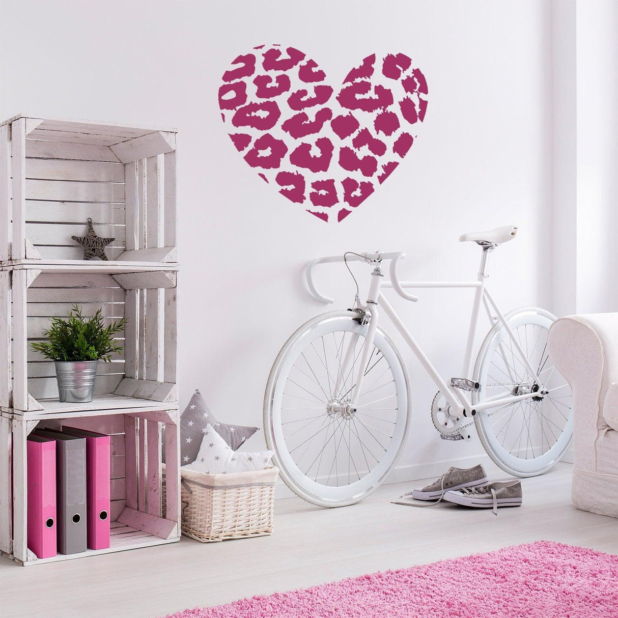 Leopard heart wall sticker in pink on a white wall above a bicycle and wooden shelf, adding stylish decor to a room.