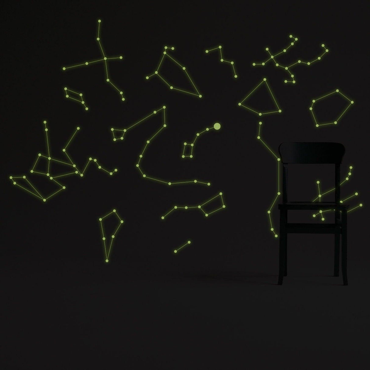 Glowing vinyl ceiling decal star map with constellations on a dark wall, featuring a black chair in the foreground.