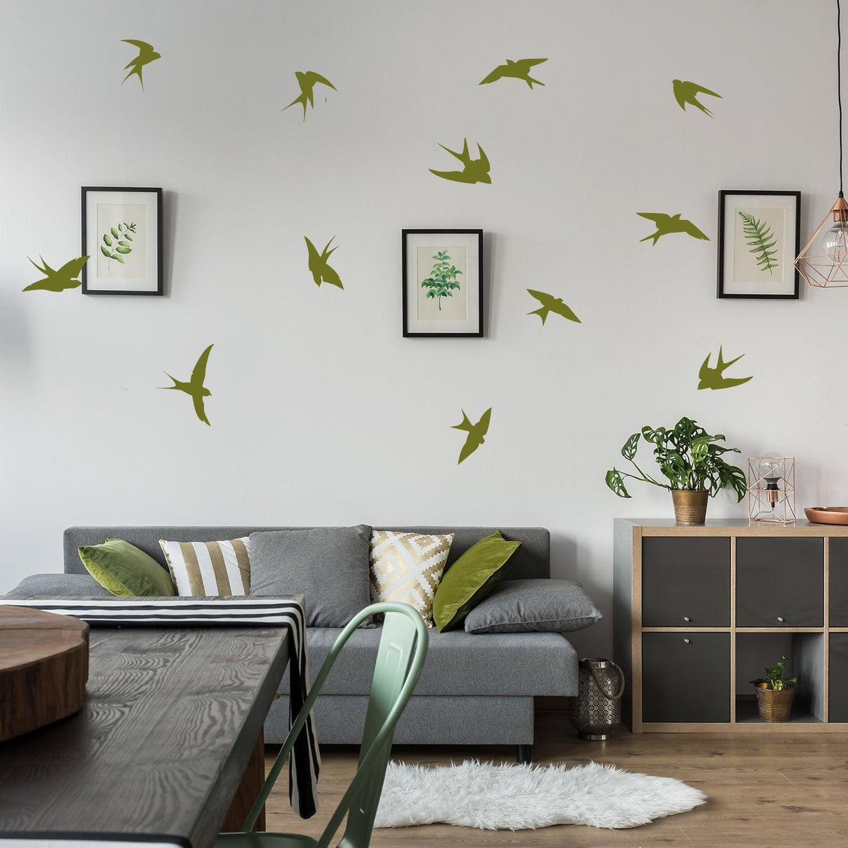 12 flock of birds wall stickers in green vinyl above a living room couch with plants and artwork, adding a nature-inspired touch.