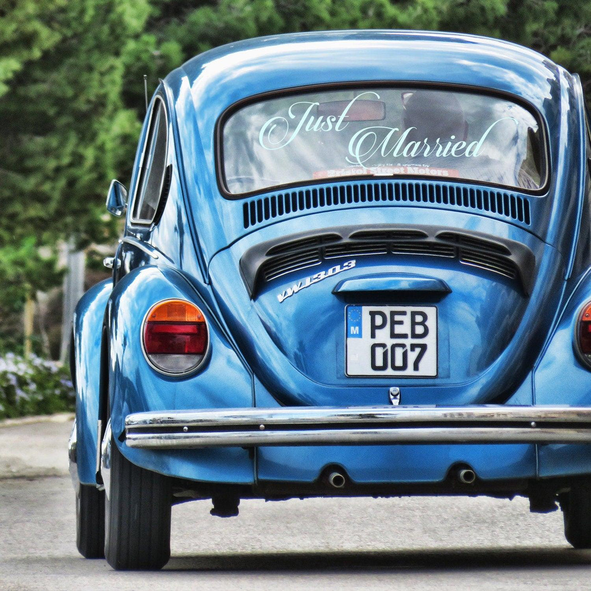 Blue vintage car with 'Just Married' sticker on rear window, perfect for wedding decor.