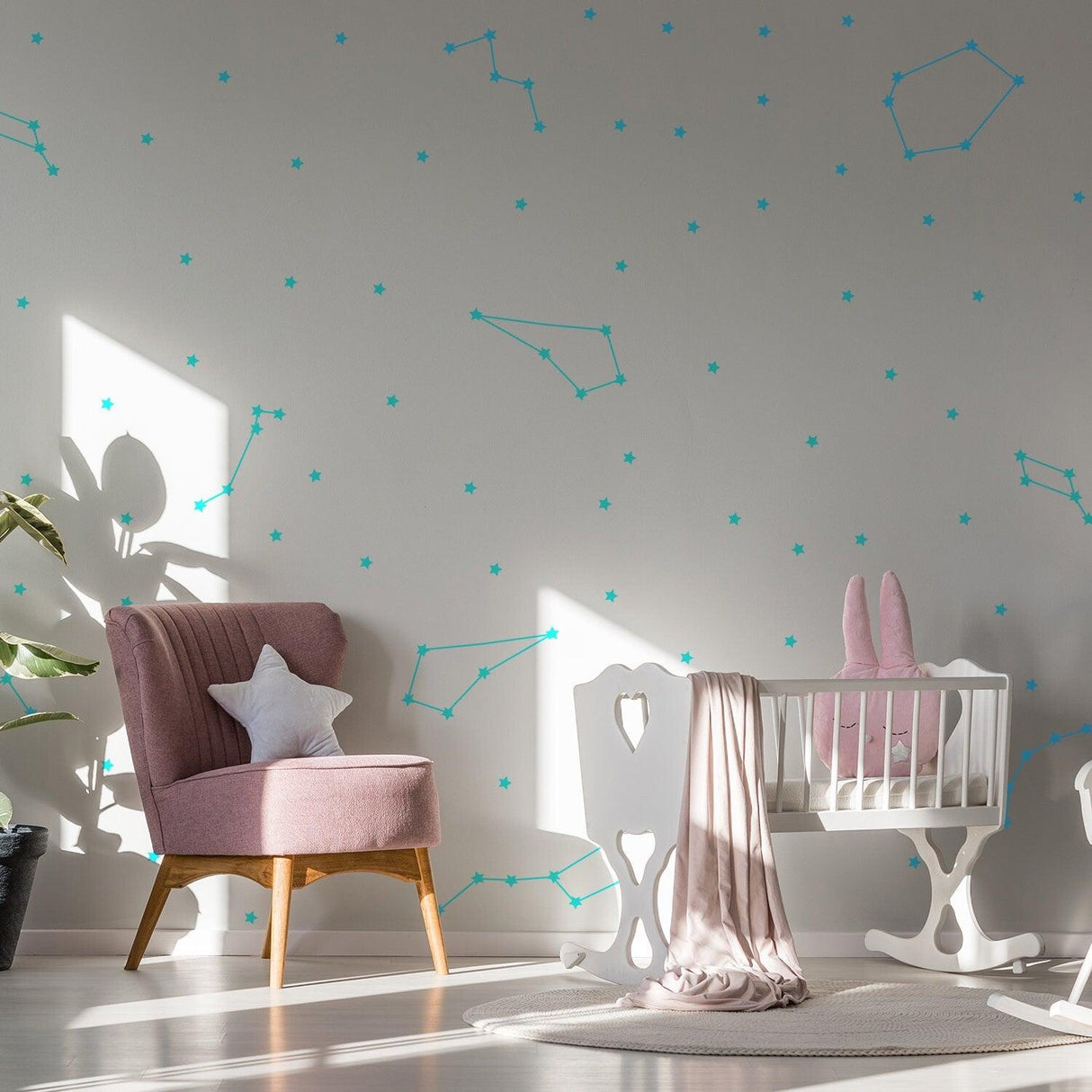 Vinyl wall stickers of zodiac constellations in a bright baby room with a pink chair and crib.
