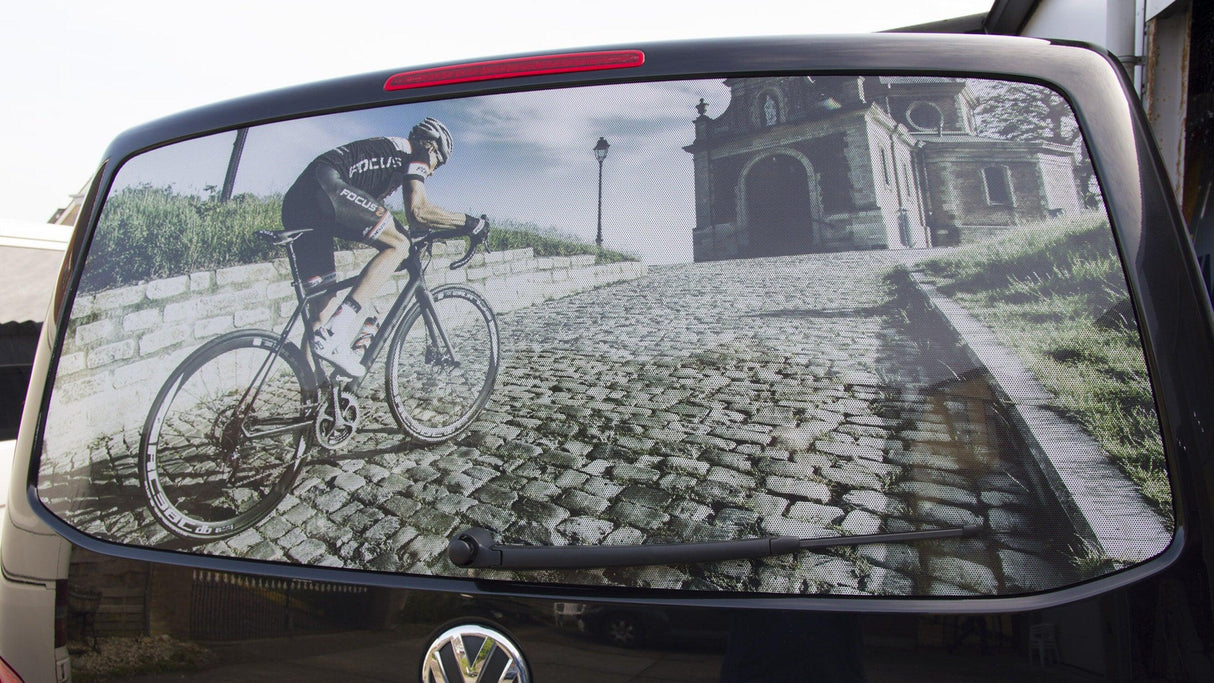 Rear window graphic featuring a cyclist riding up a cobblestone road, adding style to vehicle privacy.