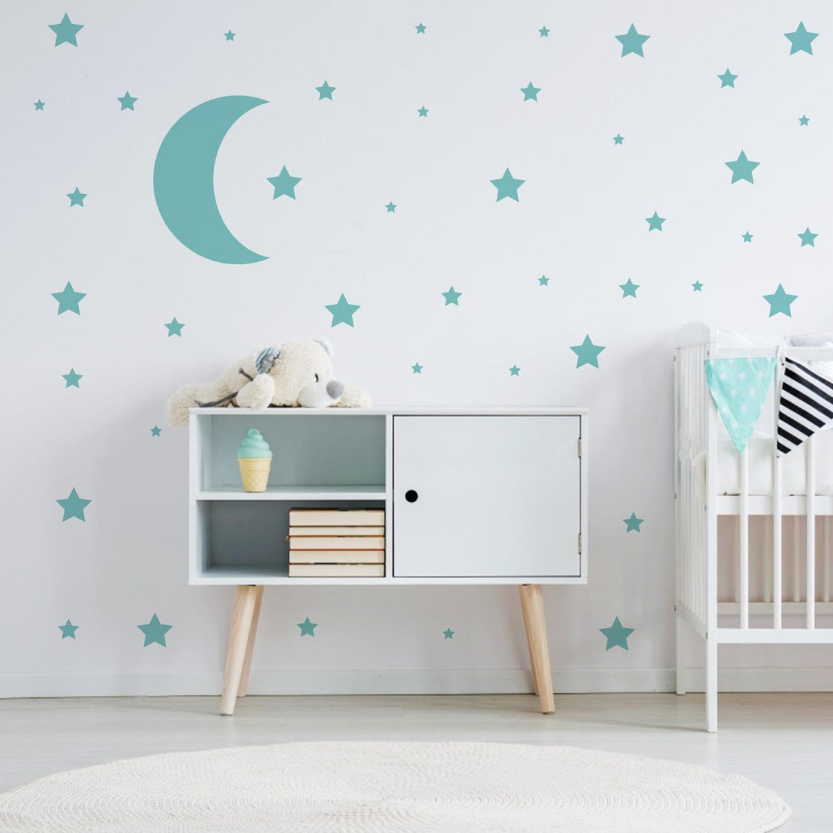 Nursery with teal star wall stickers and crescent moon decal, featuring a toy bear and modern storage cabinet.