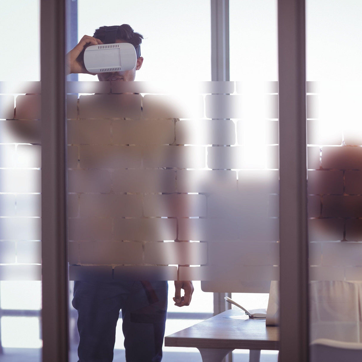 A person using a VR headset behind a frosted vinyl window decal, enhancing privacy and style in an office setting.