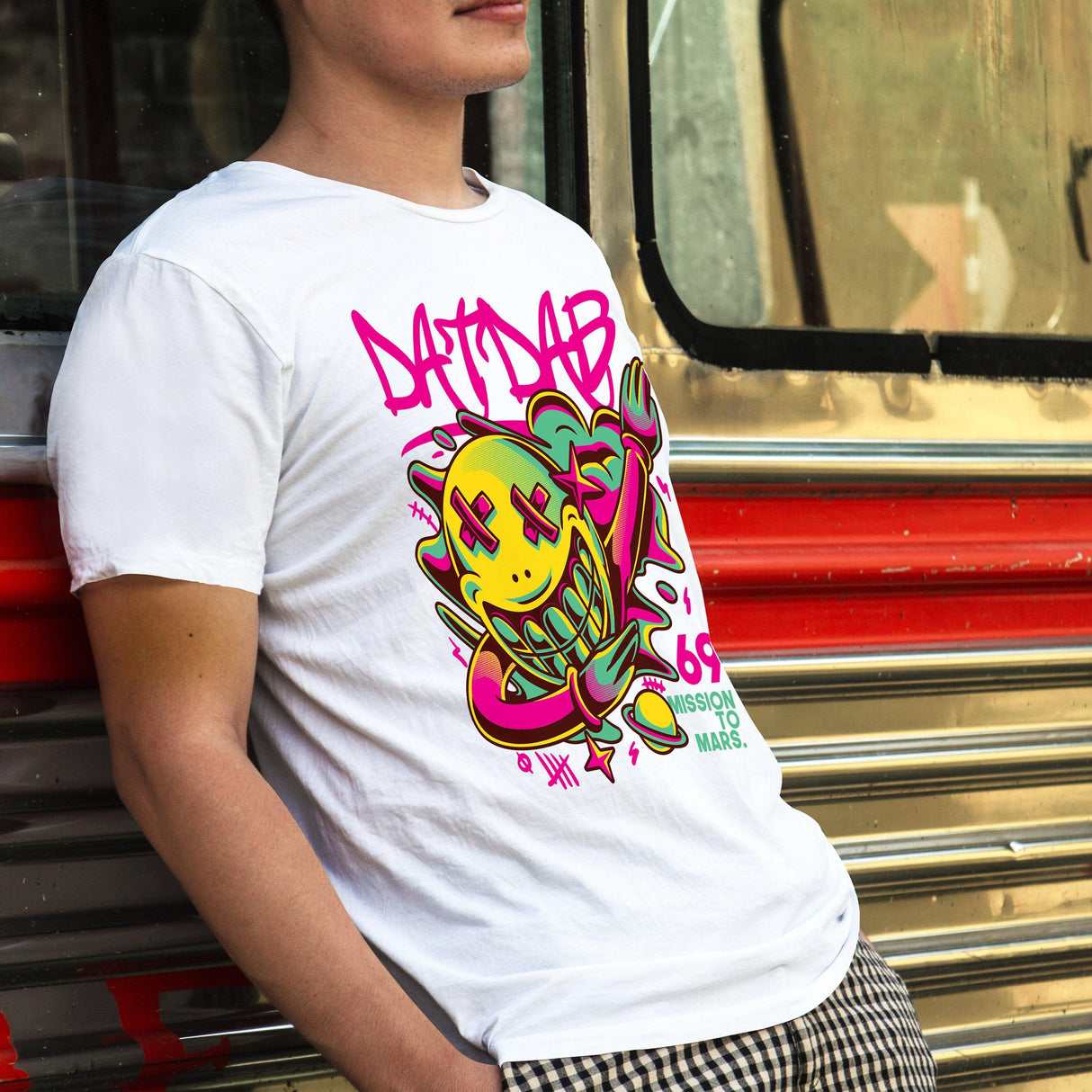 Person wearing a white t-shirt with colorful graphic design, standing next to a vintage bus.