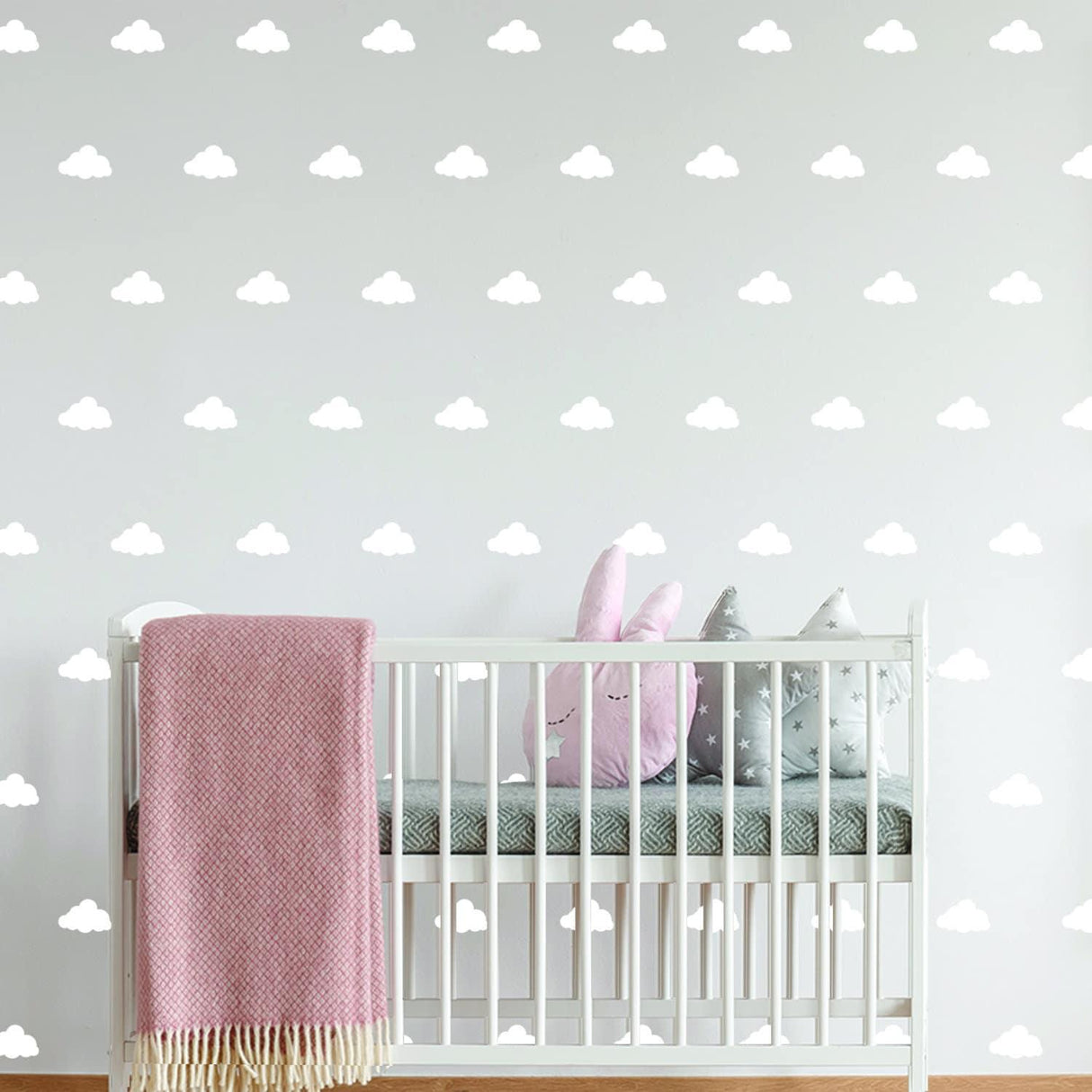 Nursery decorated with 40x cloud wall decals, featuring a crib, pink blanket, and cute plush toys.