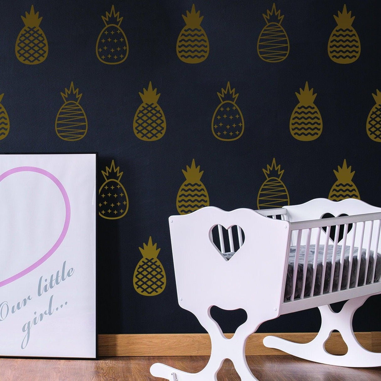 Gold pineapple wall decals on a black wall, adding elegance to a baby's bedroom with a cute white crib.