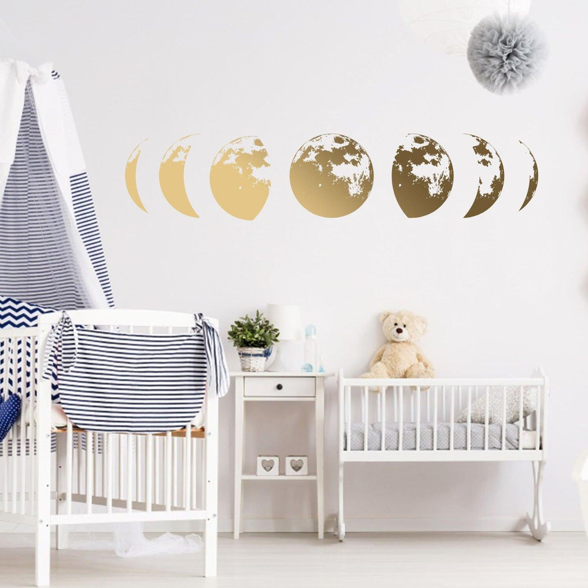 Gold moon phases wall decal in a nursery with crib and teddy bear, adding celestial decor to the room.