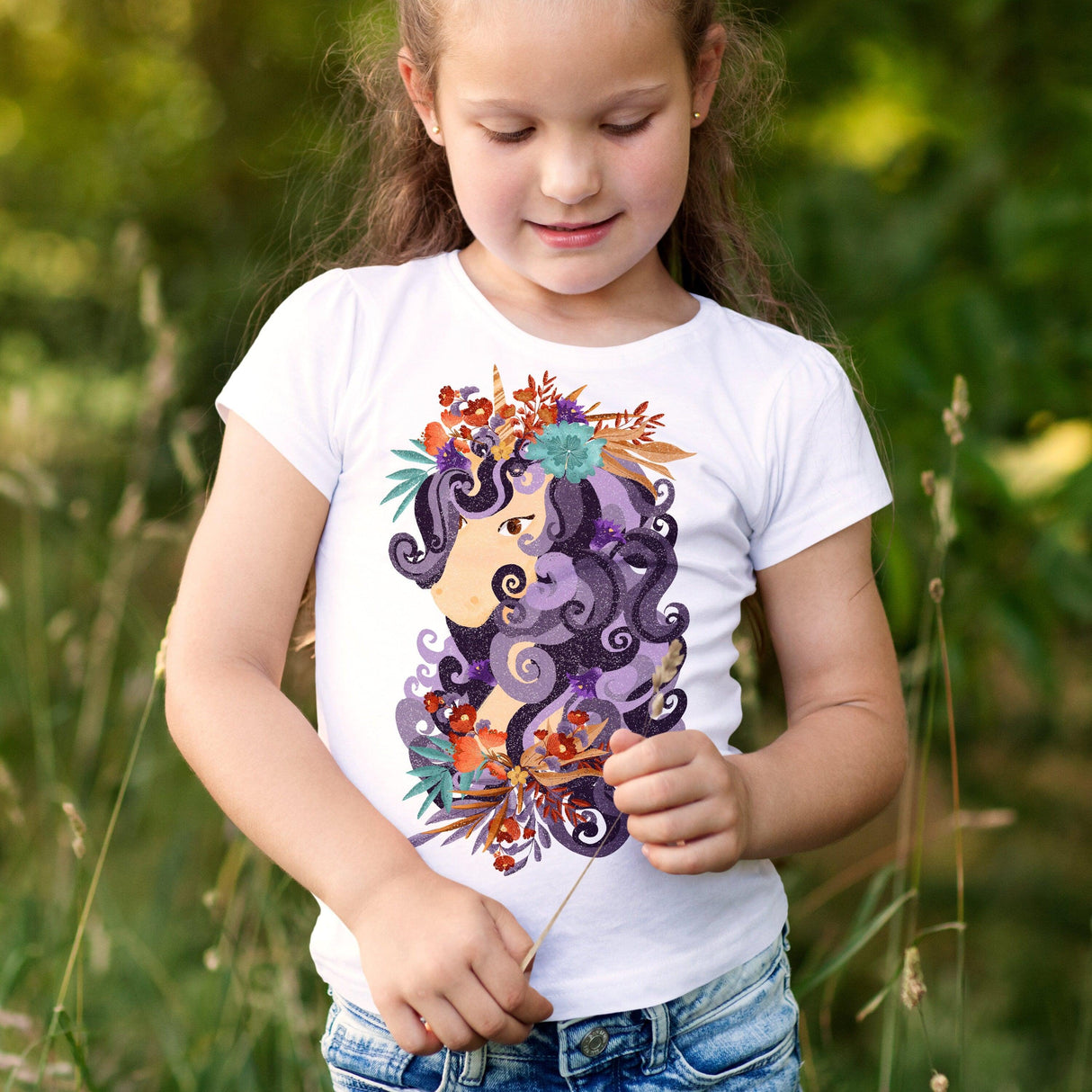 Girl wearing a white t-shirt with a colorful floral and hair design, standing in a grassy area.