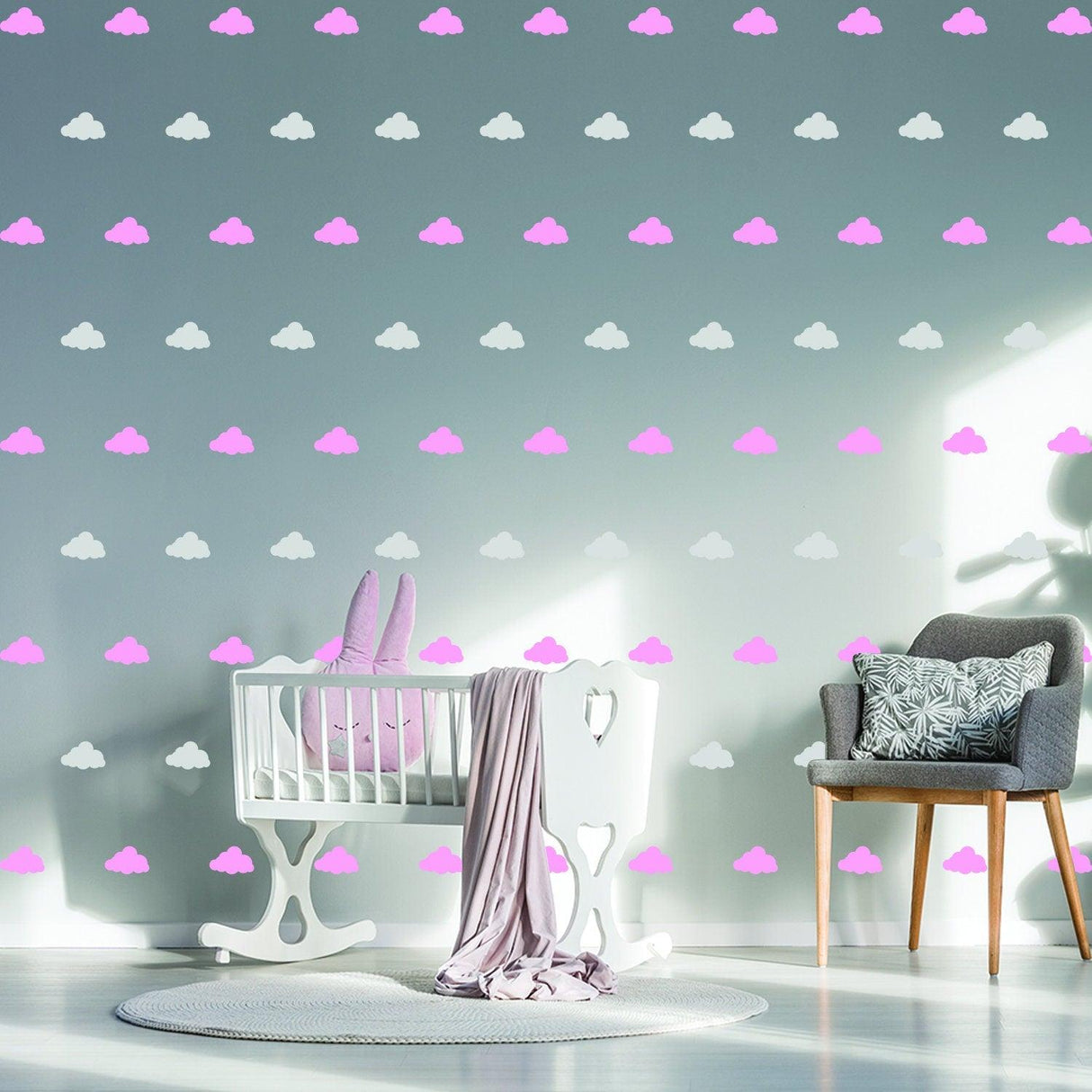 Nursery with pink and white cloud wall decals, featuring a crib and cozy chair for a whimsical baby room.
