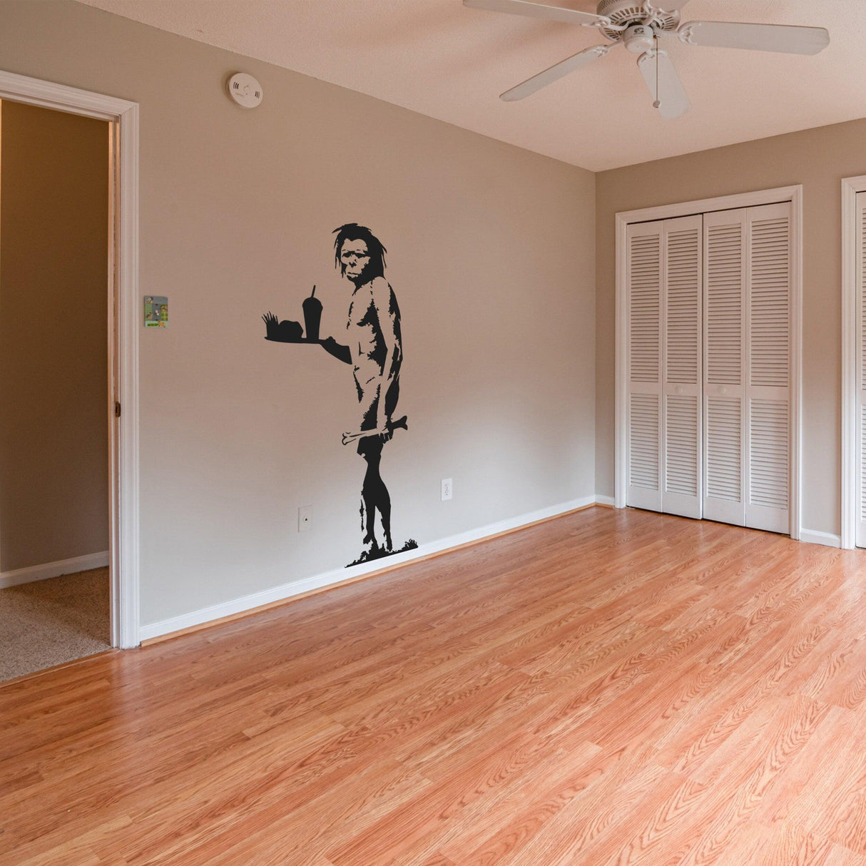 Banksy-inspired caveman vinyl wall decal on a light-colored wall in a contemporary room setting.