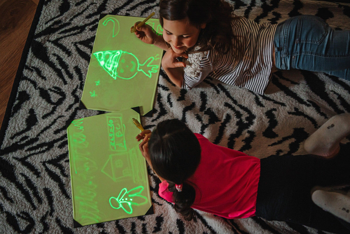 Kids drawing on a glowing light drawing board, creating colorful neon art on a zebra-patterned rug.