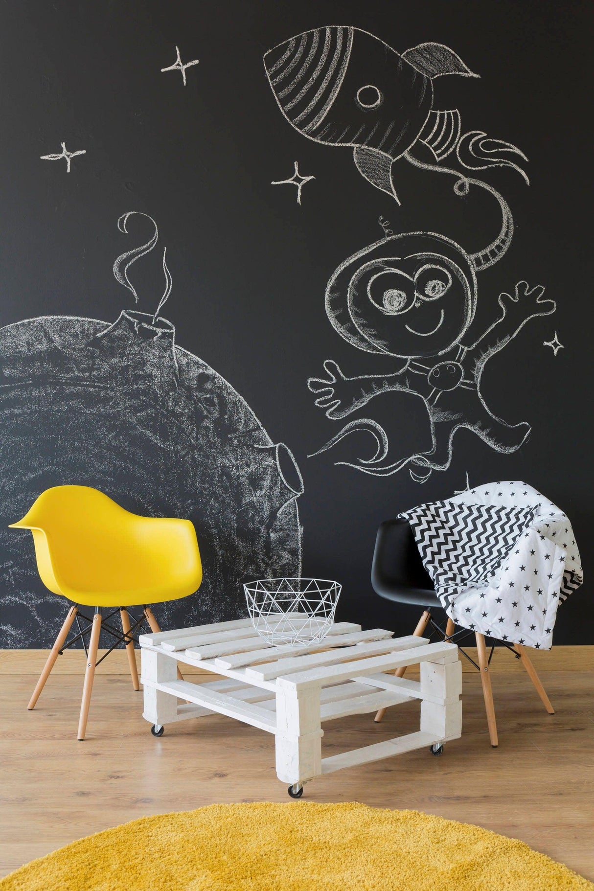 Chalkboard wall with playful rocket and astronaut illustrations, featuring modern decor and seating in a cozy room.