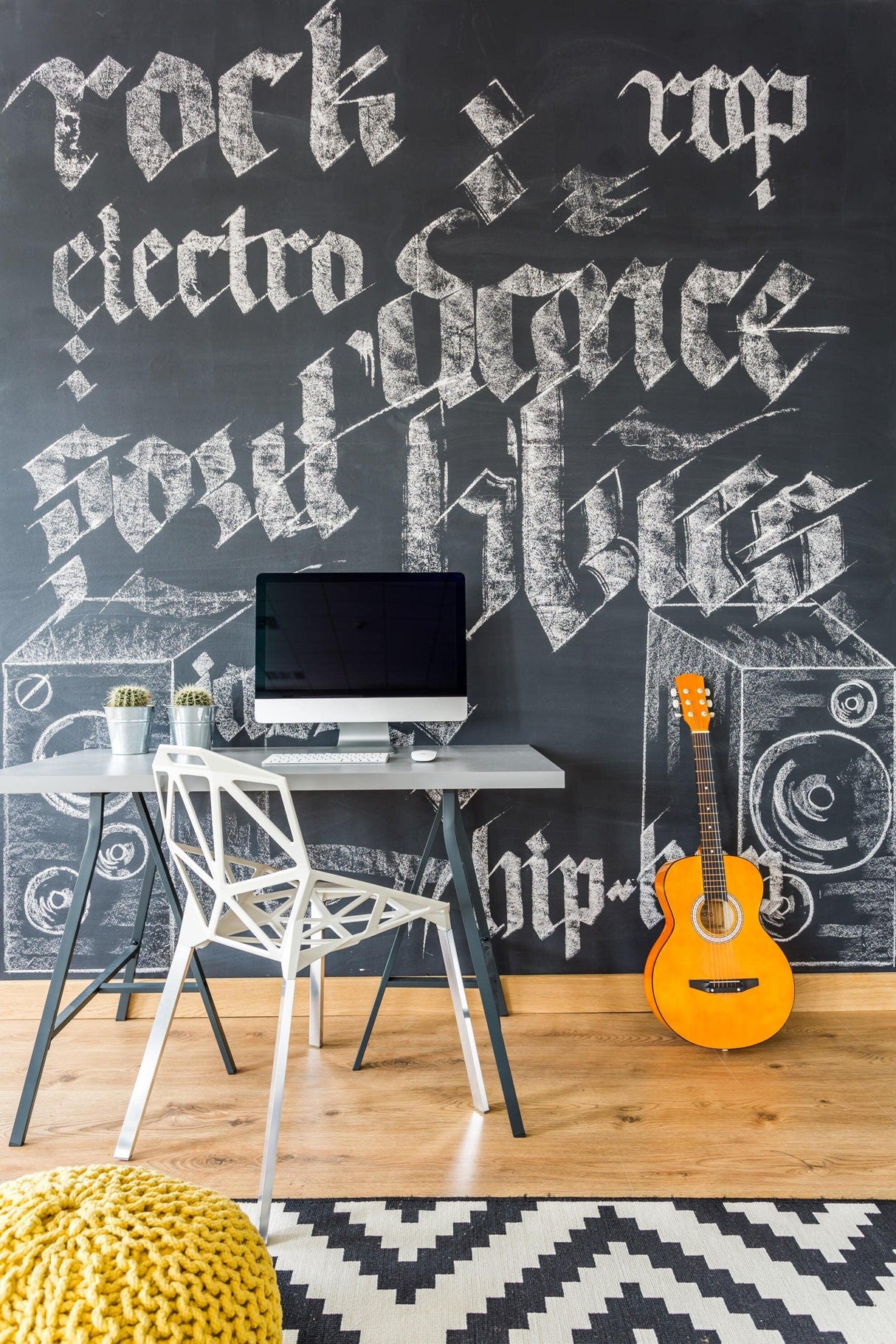 Stylish workspace with a chalkboard wall featuring music genres, desk, guitar, and modern decor.