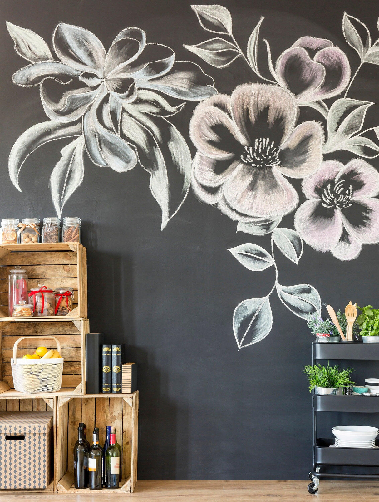 Chalkboard wall with floral designs, crates of kitchen items, and a cart with plants and wine bottles.