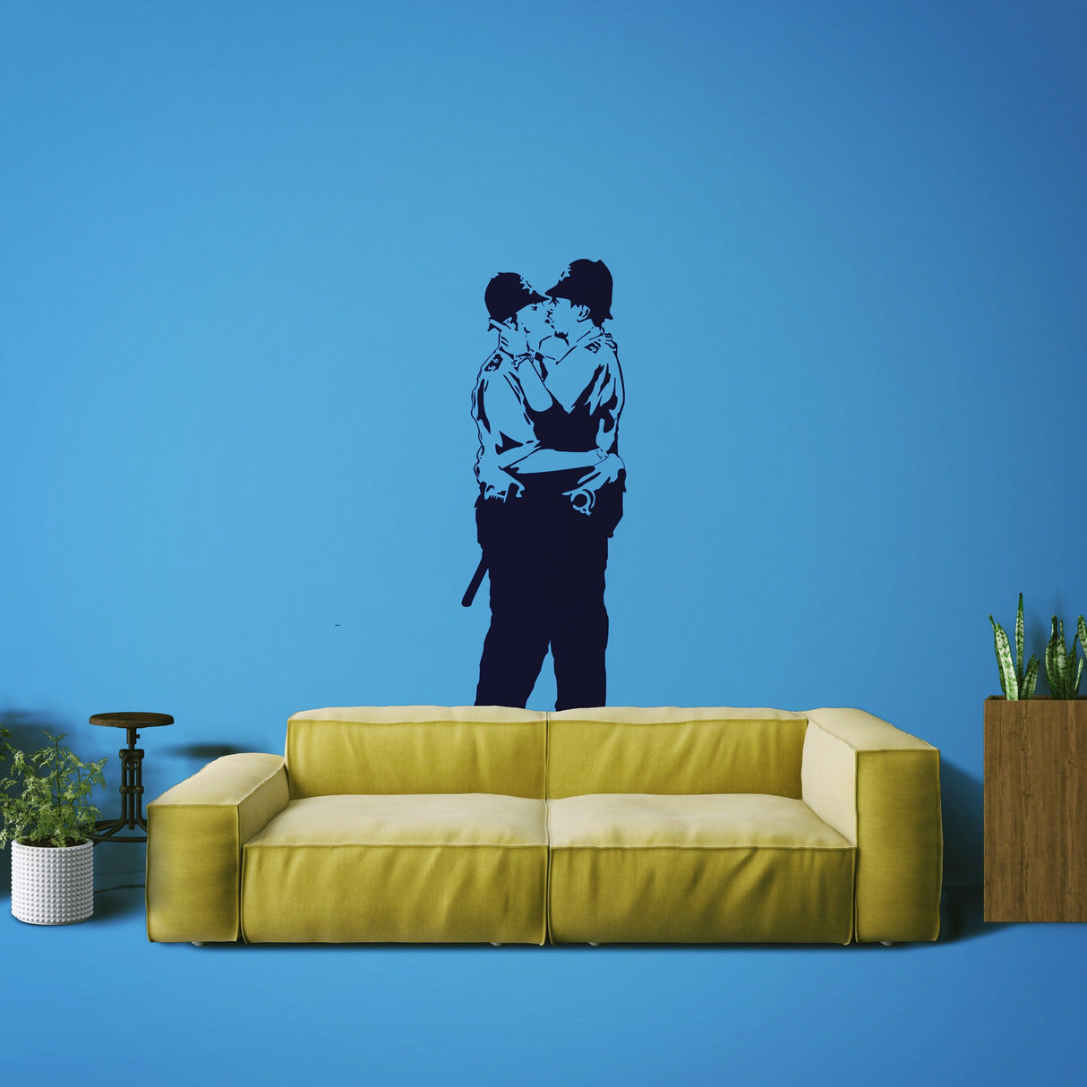Banksy Police Kissing Wall Sticker on blue wall above a yellow couch with plants, stylish street art vinyl decal.