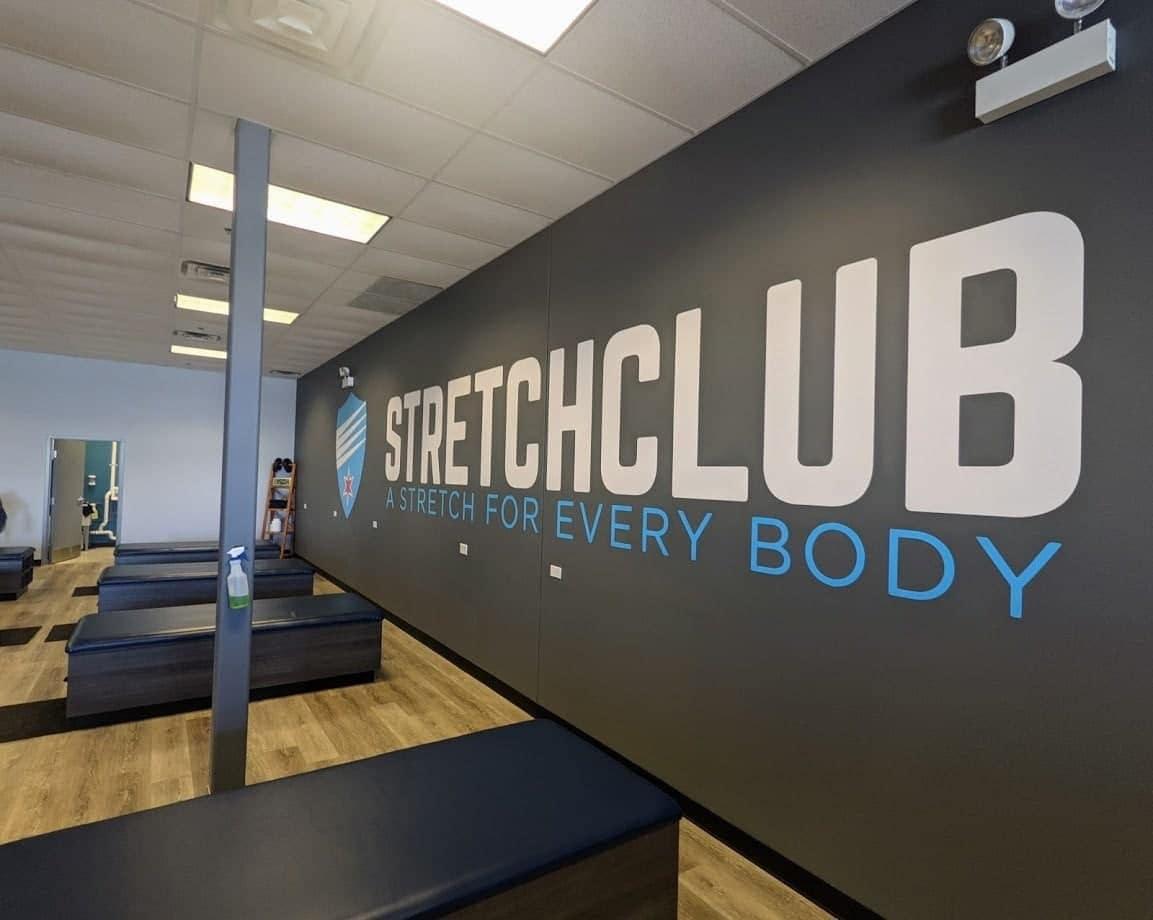 Interior of Stretch Club with large wall decal reading 'Stretch Club - A Stretch for Every Body'.