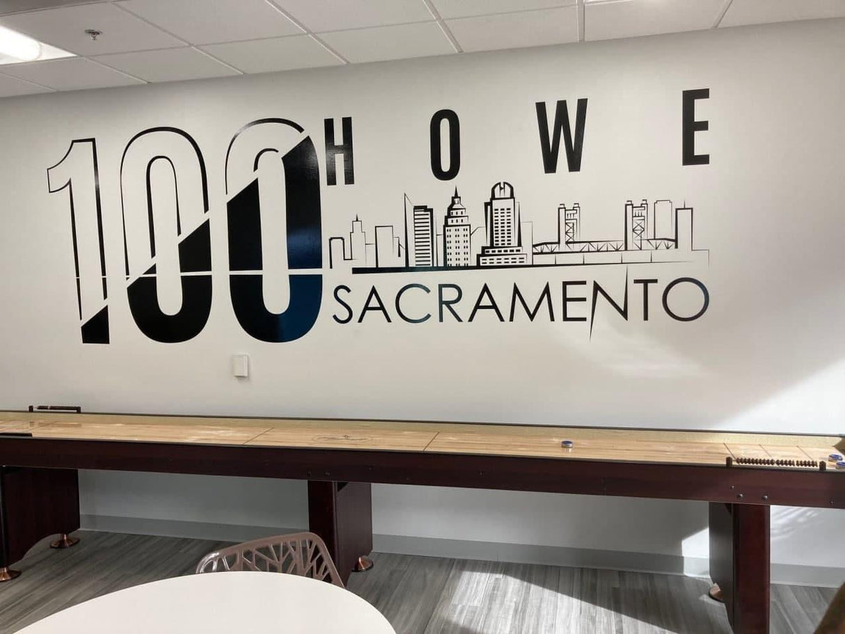 Large wall mural featuring '100 HOWE SACRAMENTO' with a city skyline design at a modern workspace.