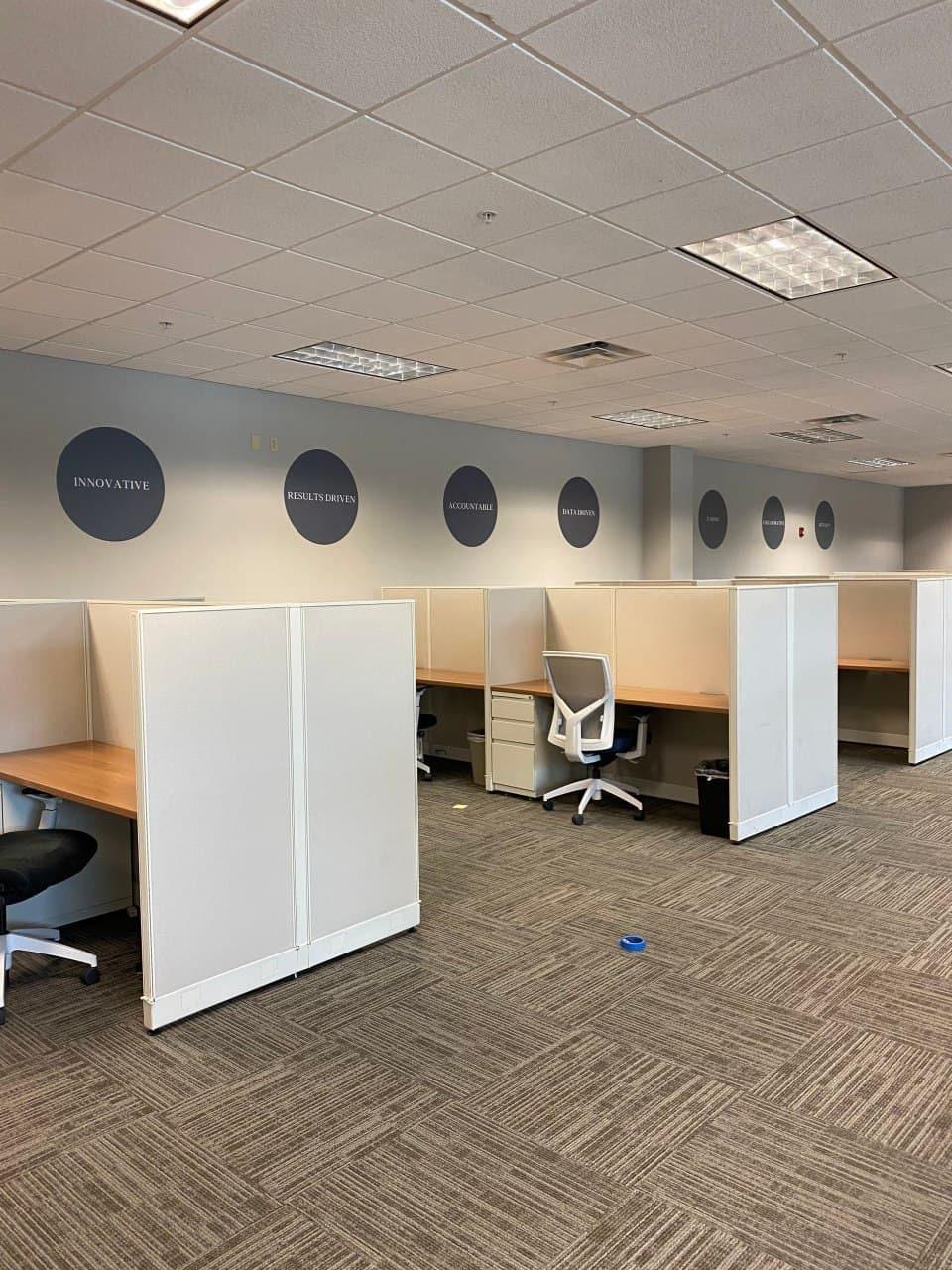Modern office cubicles with motivational wall decals like 'Innovative' and 'Creative' on the walls.
