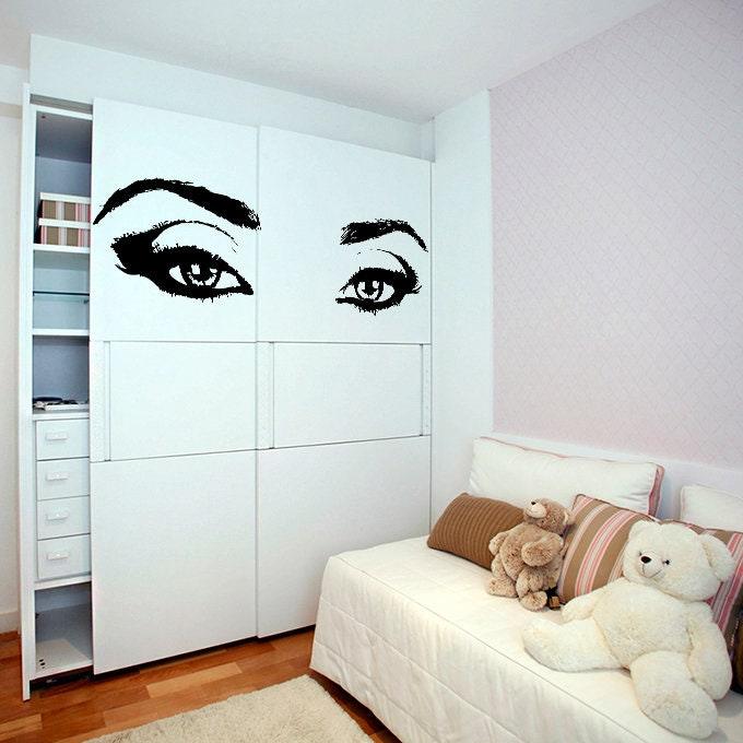 Stylish woman eyes sticker wall decor in a cozy bedroom with plush toys and neutral colors.