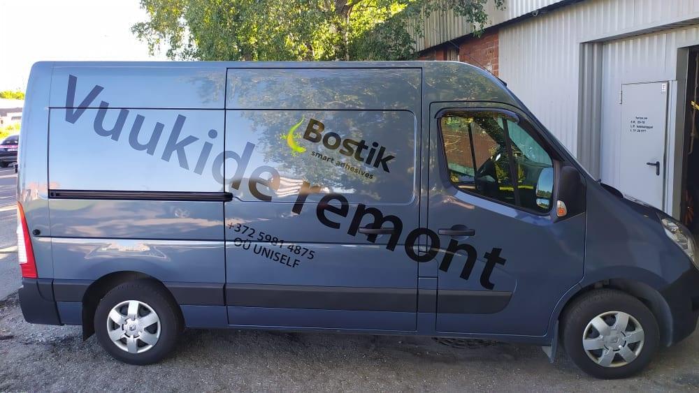 Gray delivery van with business decals for 'Bostik' and 'Vuukide remont' on the side, parked outdoors.