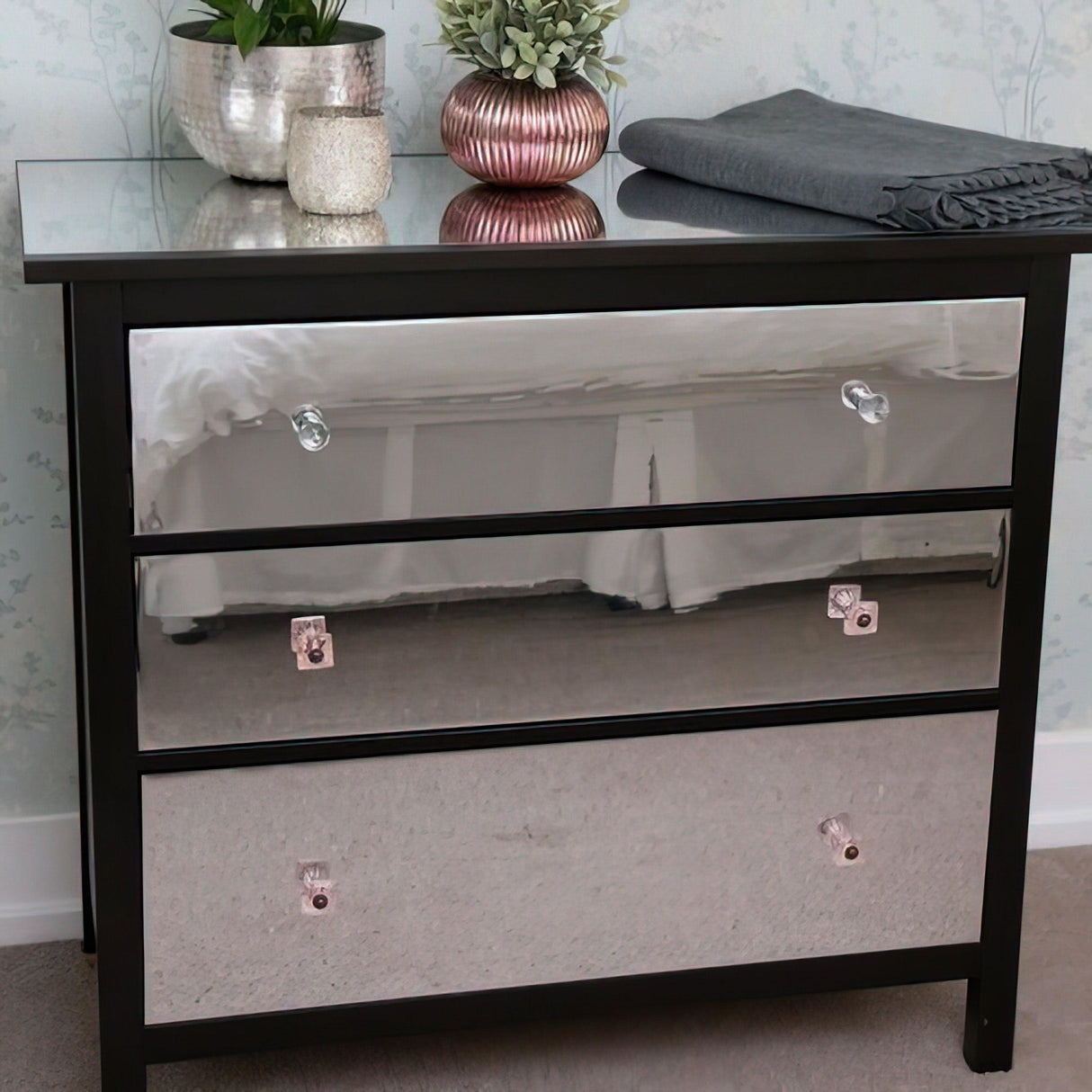 Silver chrome dresser with mirrored drawers, stylish decor plants, and a cozy blanket.