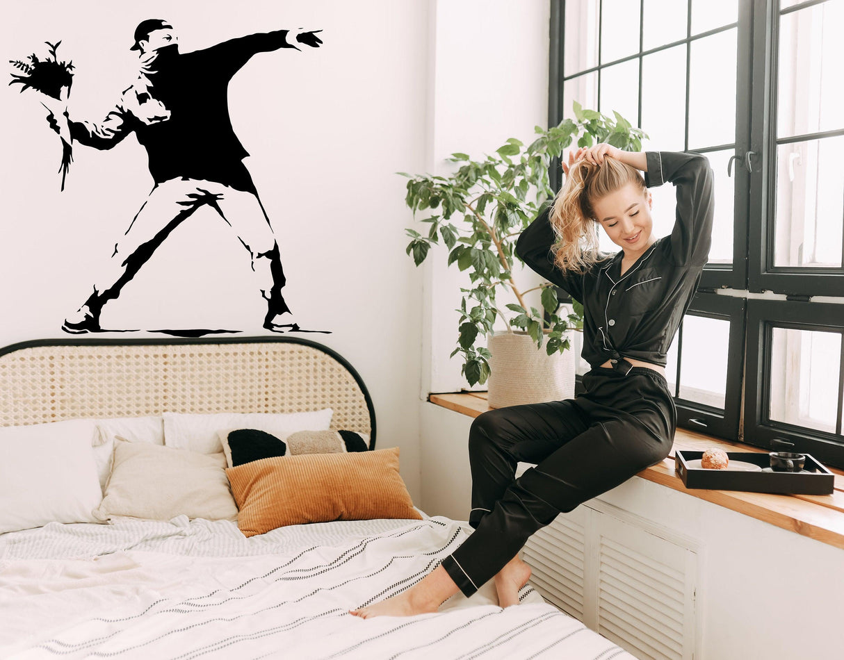 Banksy Flower Thrower wall decal in stylish bedroom with woman relaxing, adding urban art flair to decor.