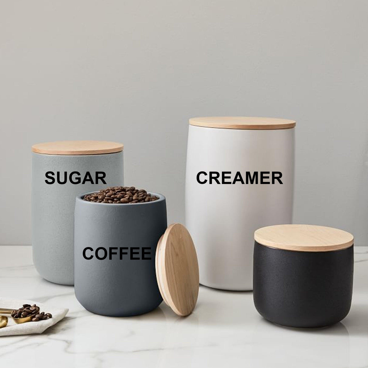 Set of four canisters labeled 'Sugar', 'Creamer', 'Coffee' on a marble countertop with wooden lids.