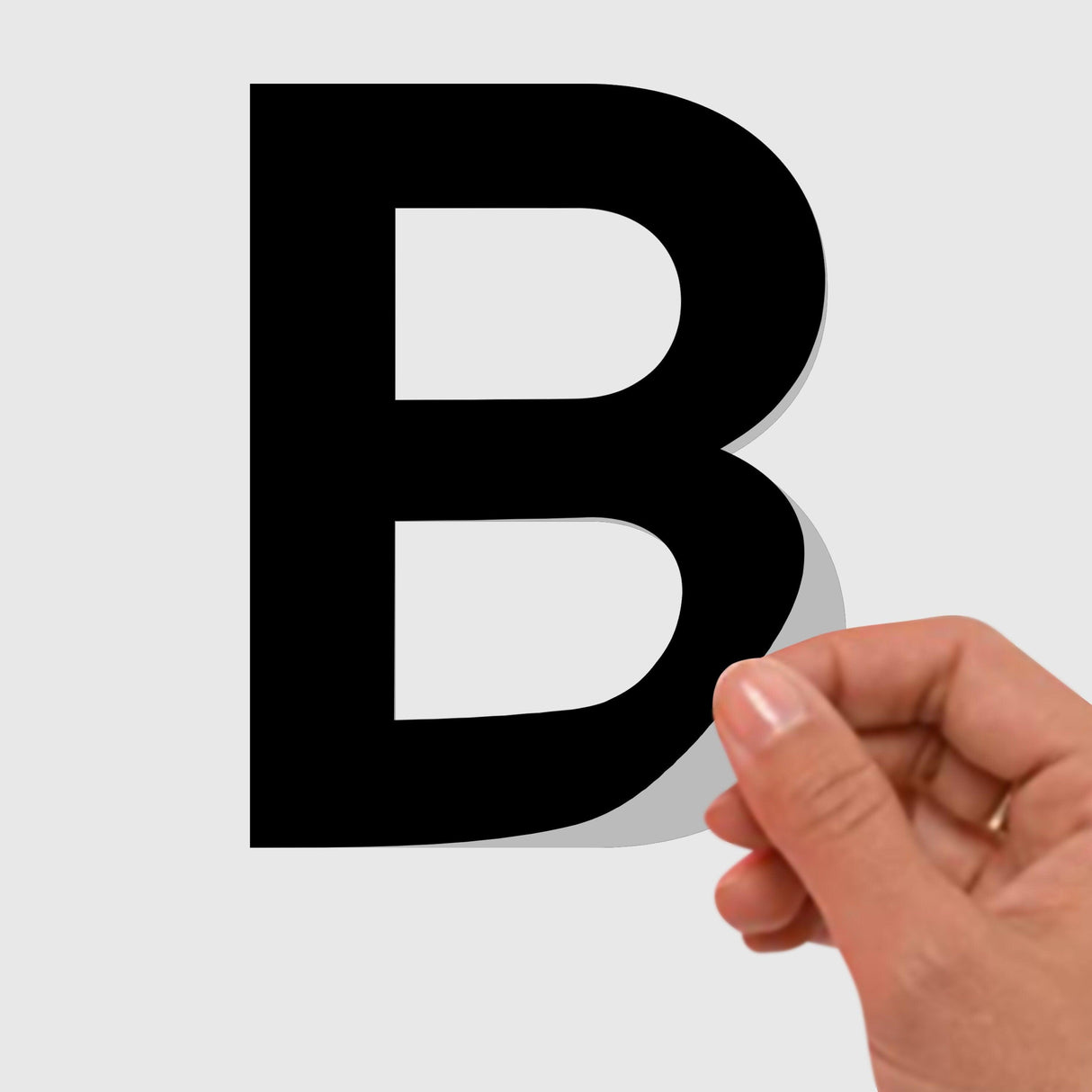 Hand peeling off a removable black letter 'B' sticker from a surface.