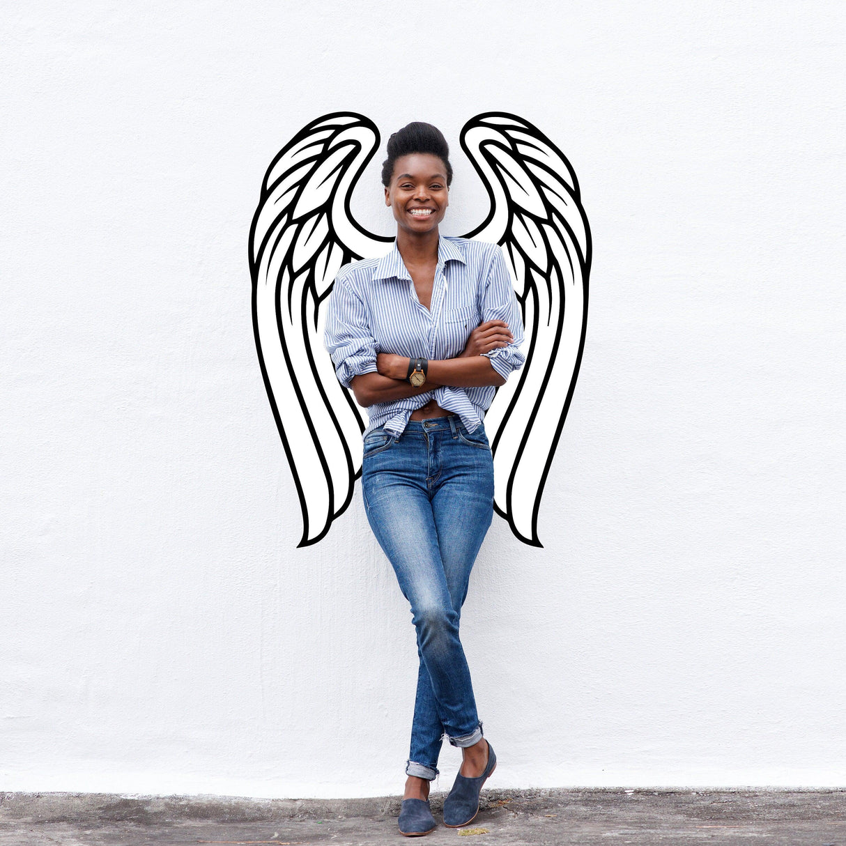 Smiling woman standing with angel wings wall decor vinyl decal on white wall, adding elegance and beauty to any space.