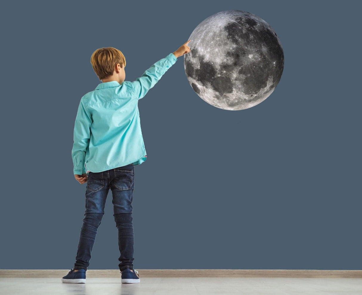 Child reaching out to touch a realistic full moon wall sticker in a stylish room.