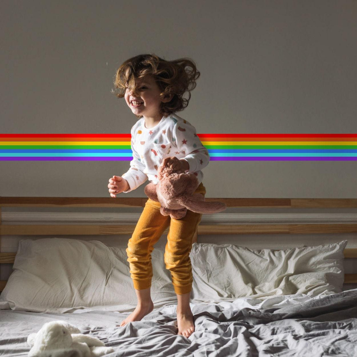 Happy child jumping on bed with rainbow border sticker on wall, showcasing vibrant colors and playful decor.
