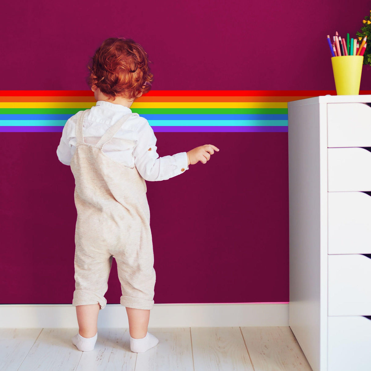Child admiring colorful rainbow stripe vinyl decal on purple wall, perfect for nursery or birthday party decoration.