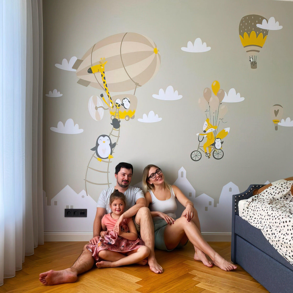 Family enjoying a whimsical nursery with penguin and fox wall stickers featuring balloons and hot air balloons.