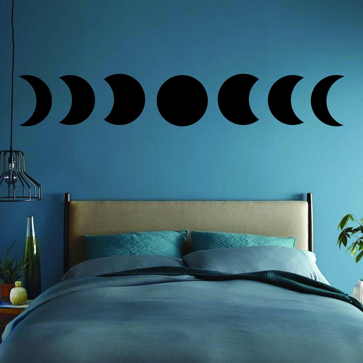 Moon Phase Wall Decor Sticker displayed above a bed on a blue wall, showcasing the phases of the moon in black vinyl.