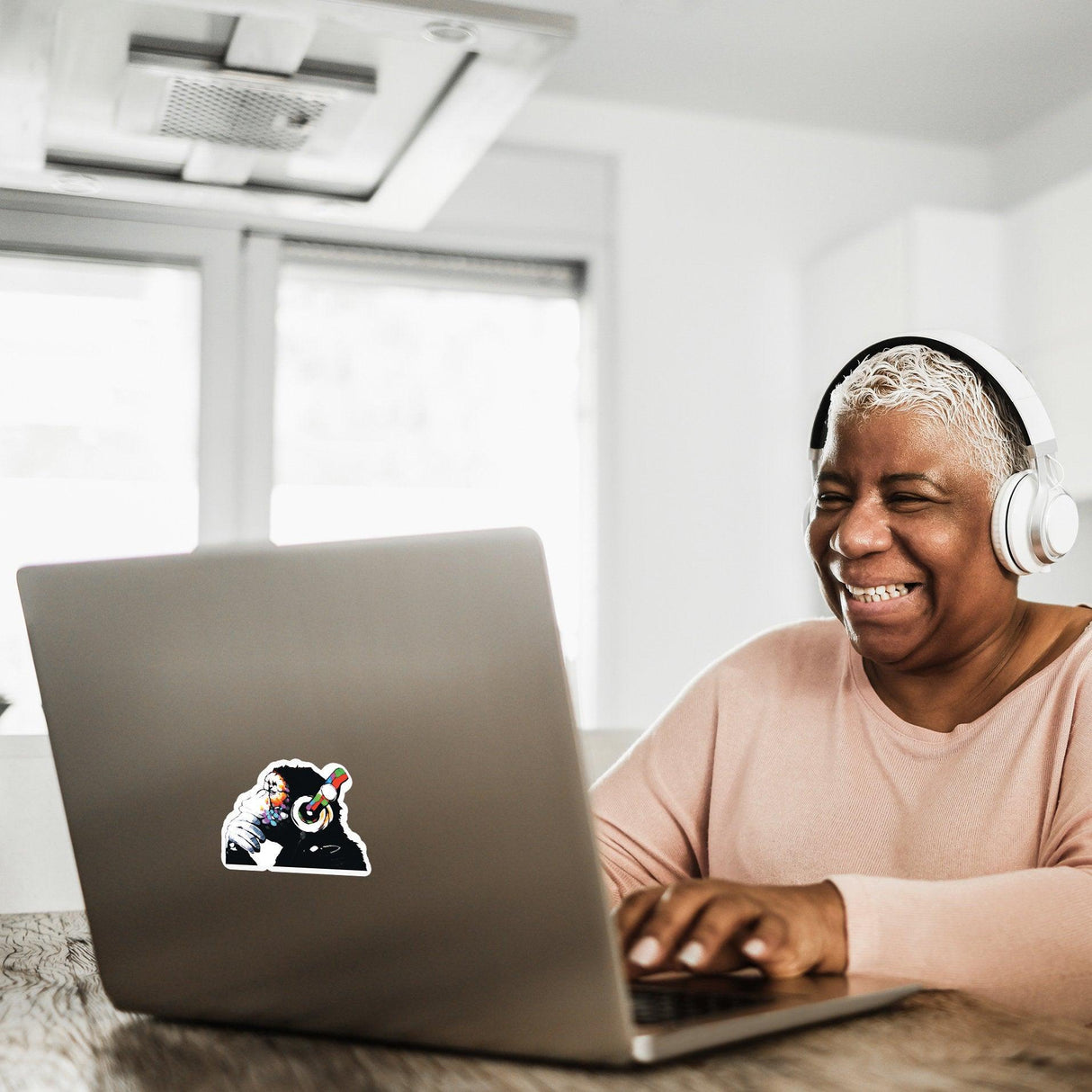 Laughing woman with headphones using a laptop adorned with a colorful Music Monkey vinyl decal.